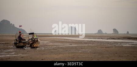 Krabi Thailand 19. Februar 2026. Zwei Longtail-Boote sitzen auf exponierten Gezeiten in der Nähe von entfernten Kalksteininseln bei Khlong Muang. Stockfoto