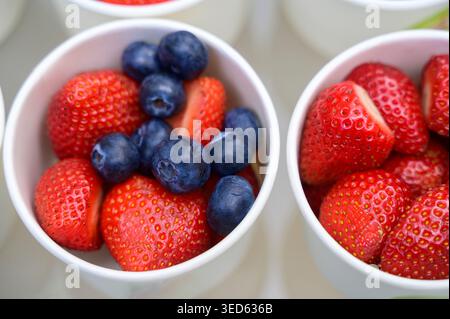 Gruppe von Plastikbechern mit frischen Erdbeeren und Heidelbeeren auf einem Marktregal. Konzept der saisonalen Beerenernte, des lokalen Lebensmittelhandels und der gesunden Orga Stockfoto