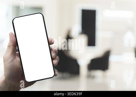 Nahaufnahme einer Hand, die einen leeren Smartphone-Bildschirm gegen einen verschwommenen Empfangsbereich hält, ideal für Apps, Kundenservice, Buchungsplattformen, Business b Stockfoto
