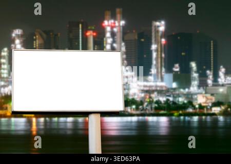 Leere weiße Reklametafel zur Werbung für Mockup vor beleuchteter Ölraffinerie und industriellem Hintergrund am Wasser bei Nacht. Beschneidungspfad Stockfoto