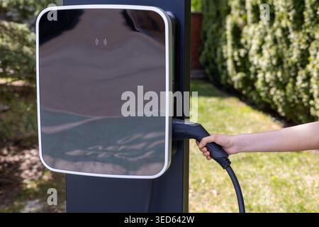 Das Ladegerät Für Elektrofahrzeuge Mit Der Hand Anschließen. Nahaufnahme einer Hand, die ein Elektrofahrzeug-Ladekabel an einer Außenstation verbindet, zeigt sauber Stockfoto