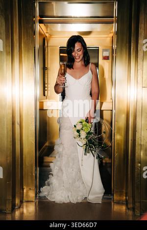 Braut feiert mit Champagner und hält Hochzeitsstrauß im Aufzug Stockfoto