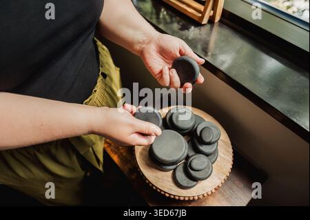 Hände halten und sortieren Massagesteine auf Holztablett für Fenster Stockfoto