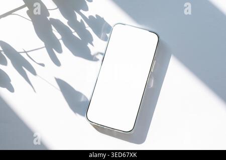 Minimale flache Lage mit Mobiltelefon und hinterlässt Schatten auf weißem Hintergrund. Draufsicht, Modell. Stockfoto