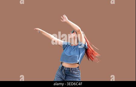 Fröhliche trendige Frau mit rotem Haar, die auf trendigem farbigem Wandhintergrund auf der Straße tanzt. Mocha Mousse - Farbe des Jahres 2025 Stockfoto