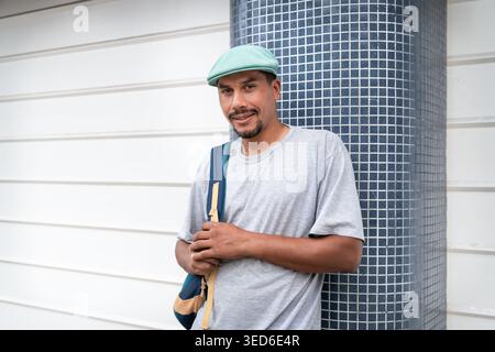 Porträt eines jungen lateinamerikanischen hispanischen Mannes mit Rucksack, der seine Kappe anpasst, während er auf einer Wohnstraße steht. Stockfoto