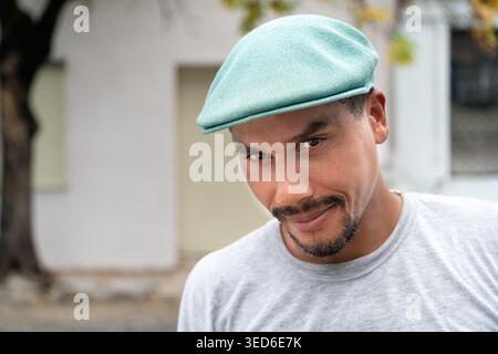 Ein Latino-Mann mit flacher Mütze, der in die Kamera schaut, mit einem Baum mit Herbstlaub im Hintergrund. Kopierbereich Stockfoto
