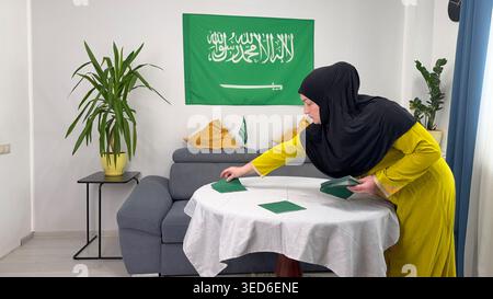 Erwachsene muslimische Frau aus dem Nahen Osten in schwarzem Hijab und gelbem Kleid, die einen Tisch für Iftar zu Hause arrangiert. Stockfoto