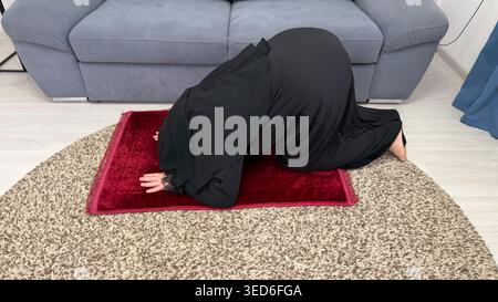 Nahaufnahme einer muslimischen Frau im Hijab, die während des Gebets zu Hause Prostration ausführt. Spiritualität und religiöse Hingabe. Stockfoto