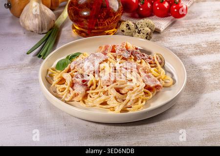Appetitliche Spaghetti Carbonara serviert auf weißem Teller. Eine reichhaltige cremige Sauce umhüllt Nudeln, garniert mit knusprigem Speck und frischem Basilikum. Rustikaler Hintergrund Stockfoto