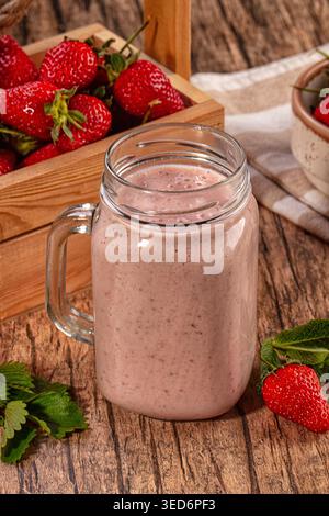 Gesunder Erdbeere-Smoothie im Glas auf rustikalem Holztisch. Frisches rosafarbenes Getränk mit Reifen roten Beeren und grüner Minze. Gesundes Frühstück oder Snack Stockfoto