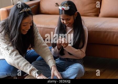 Verschiedene Mutter und Tochter sitzen zu Hause mit Geweih-Haarbändern, Tochter mit Handwerkskunst Stockfoto