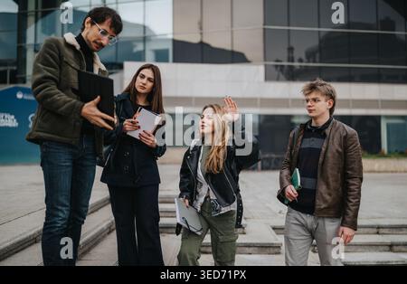High-School-Schüler diskutieren einen Auftrag mit einem Lehrer vor einem modernen Schulgebäude Stockfoto