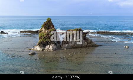 Atemberaubende Drohnenaufnahme, die einen tropischen Strand in Sawarna, Indonesien, mit berühmten großen Felsformationen, türkisfarbenen Meereswellen und unberührten Elementen einfängt Stockfoto