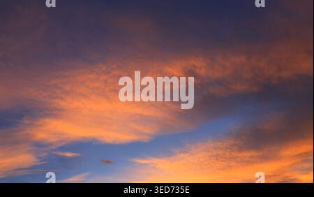 Der Himmel ist voller Wolken, die von den warmen Orange- und Rosa-Tönen beleuchtet werden und sich bei Sonnenuntergang mit tiefen Blautönen kontrastieren Stockfoto
