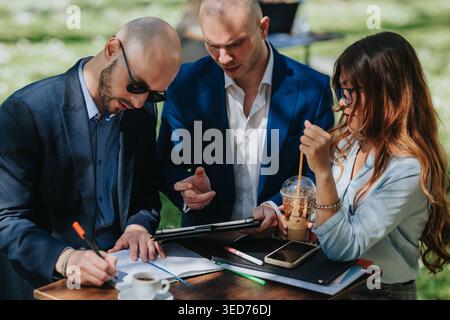 Geschäftstreffen im Freien mit Kollegen, bei dem Dokumente und Tablets bei Kaffee im Park diskutiert werden Stockfoto
