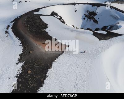 Aus der Vogelperspektive auf den schneebedeckten Vulkankrater am Südhang des Ätna mit Menschen, die auf einem Pfad in Nicolosi, Sizilien, Italien, spazieren gehen. Stockfoto