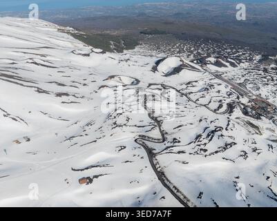 Aus der Vogelperspektive auf die Versante Sud dell' Ätna mit schneebedeckten Vulkankratern und gewundenen Bergstraßen in Nicolosi, Sizilien, Italien. Stockfoto