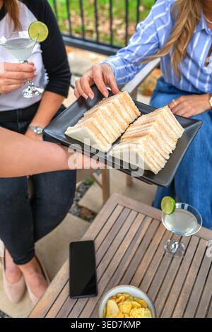 Nicht erkennbare Frauen, die sich auf einer Party treffen und Sandwichvorspeisen und Cocktails auf der Terrasse servieren Stockfoto