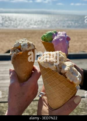 Drei Frauen, die an einem Sandstrand auf einer Promenade stehen und an einem Frühlingstag traditionelle dänische Eiskegel essen, Hjerting, Esbjerg, Jütland, Dänemark Stockfoto