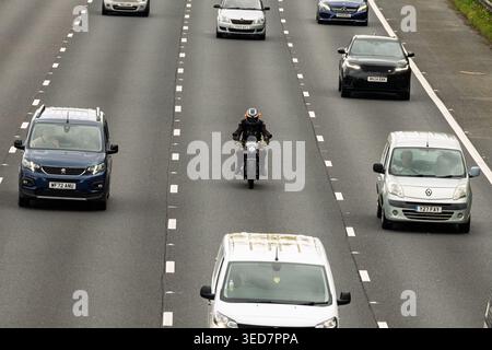 Auf einem stark frequentierten M6 North Highway in Warrington schlängelt sich ein einsamer Motorradfahrer geschickt durch einen Strom schnell fahrender Fahrzeuge. Stockfoto