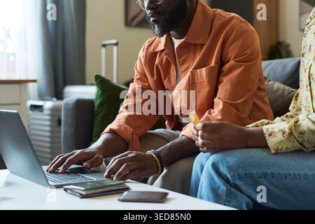 Afroamerikanisches junges Erwachsenenpaar, das Reisen mit Laptop und Kreditkarte Bucht und sich auf die Reise mit Gepäck in der Nähe vorbereitet. Ideal für Urlaubsplanung, Online-Buchung, Reisebudget-Inhalte Stockfoto