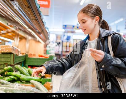 Mädchen, Das Gurken Im Gemüsebereich Des Supermarktes Wählt Stockfoto
