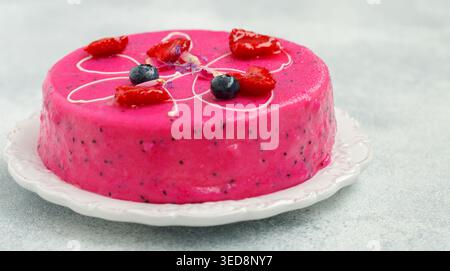 Hausgemachter Mousse-Kuchen mit Pitahaya und frischen Beeren. Dekoriert mit Heidelbeeren, Himbeeren, Blumenblättern und weißer Schokolade auf hellem Hintergrund Stockfoto
