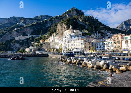 Amalfi Harbour Waterfront mit Tetrapoden Breakwater, Hügelgebäuden und dramatischer Bergkulisse, Amalfiküste, Kampanien, Italien Stockfoto