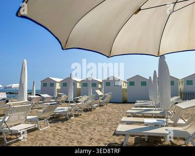 Sonnendurchfluteter Sandstrand mit Liegestühlen und Sonnenschirmen, Blick auf saubere weiße Strandhütten am Meer in Lido di Venezia, Italien. Stockfoto