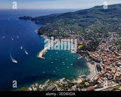 Blick aus der Vogelperspektive auf den Hafen und die farbenfrohen Gebäude entlang des Ufers mit Booten, die in der blauen Bucht und den üppigen grünen Hügeln verankert sind Santa Margherita Ligure, Stockfoto