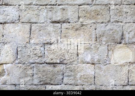 Alte Beige Steinmauerstruktur. Verwitterte beige Steinwand mit rauen Blöcken und Mörtellinien, ideal für Architektur, Hintergrund oder Textur. Stockfoto