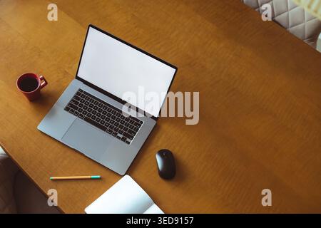 Eine Person benutzt zu Hause einen Laptop auf einem Holztisch. Eine Tasse Kaffee steht neben dem Laptop. Ein Stift und ein Notizbuch liegen ebenfalls auf dem Tisch. Die Einstellung Stockfoto