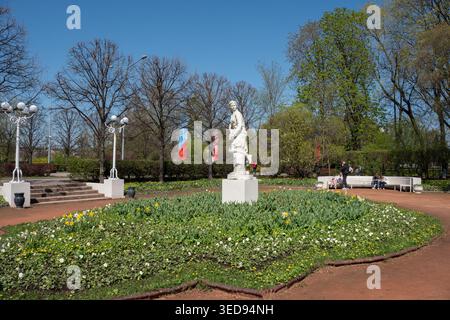 Moskau, Russland - 3. Mai 2026: Statue im Gorki-Park umgeben von Blumenbeeten, Bäumen und Wanderwegen unter klarem Himmel bei Frühlingstag. Stadtdokument Stockfoto