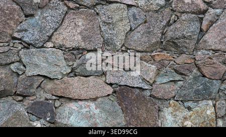 Wunderschönes Rohsteinwerk aus massivem Granitfelsen und kleinen Kieselsteinen, ein Bruchstück einer Mauer oder eines Zauns aus Naturstein Stockfoto