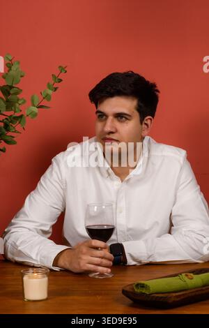 Mann sitzt am Tisch und hält Weinglas, entspannter Lifestyle und Restaurantkonzept mit warmen Tönen Stockfoto
