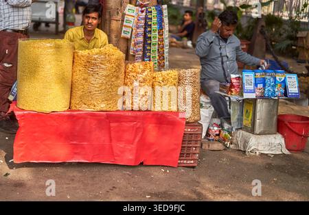Ein Straßenhändlerstand zeigt große durchsichtige Plastiktüten, gefüllt mit verschiedenen gelben und orangefarbenen Snacks, Chips und Nüssen, die auf einem Roten angeordnet sind Stockfoto