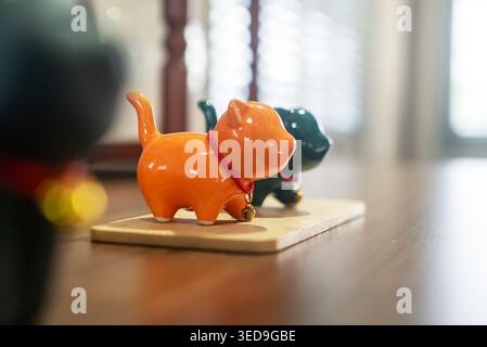 Zwei Keramikkatzenfiguren in Orange und Grün sind auf einem Holzsockel mit verschwommenem Hintergrund ausgestellt, die eine gemütliche Indoor-Szene einfangen und betonen Stockfoto
