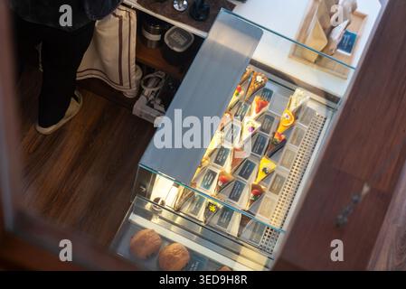 Diese Vitrine aus Glas zeigt eine Vielzahl von bunten Pralinen, Süßigkeiten, Keksen und Snacks, die ordentlich für den Einzelverkauf in einem gemütlichen Geschäft setti arrangiert werden Stockfoto
