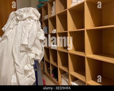Benutzte Frottiertücher in einem speziellen Korb in der Nähe leerer Regale, isoliert auf hellem Hintergrund. Stockfoto
