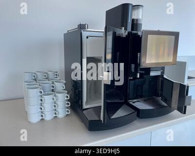 Moderne kommerzielle Espressomaschine mit offener Tür und Stapel weißer Keramikbecher auf einer Theke, professionelle Catering-Ausrüstung Stockfoto