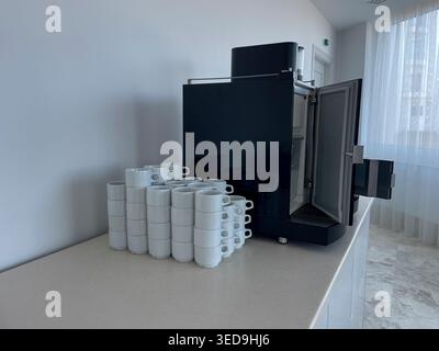 Moderne kommerzielle Espressomaschine mit offener Tür und Stapel weißer Keramikbecher auf einer Theke, professionelle Catering-Ausrüstung Stockfoto