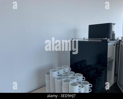 Moderne kommerzielle Espressomaschine mit offener Tür und Stapel weißer Keramikbecher auf einer Theke, professionelle Catering-Ausrüstung Stockfoto