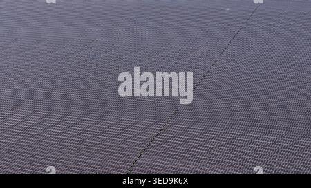 Eine Luftperspektive erfasst eine riesige Reihe dunkelblauer Solarpaneele, die in einem Gittermuster angeordnet sind und sich über den Rahmen erstrecken. Die gleichmäßigen Reihen von Phot Stockfoto