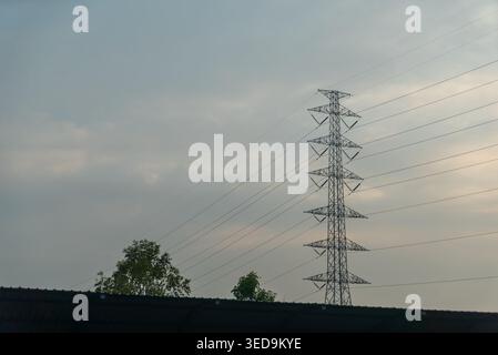 Ein Hochspannungsturm steht hoch vor einem bewölkten Himmel und zeigt die Mischung aus Technologie und Natur in einer urbanen Landschaft bei Sonnenuntergang. Stockfoto