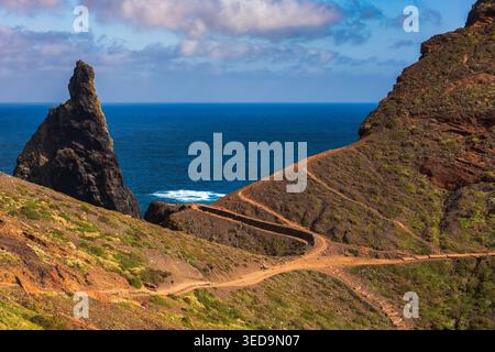 Atemberaubende vulkanische Küste in Madeira mit steilen Klippen, einem markanten Felsenpinnakel, gewundenen Küstenpfad und türkisfarbenem Atlantik Stockfoto