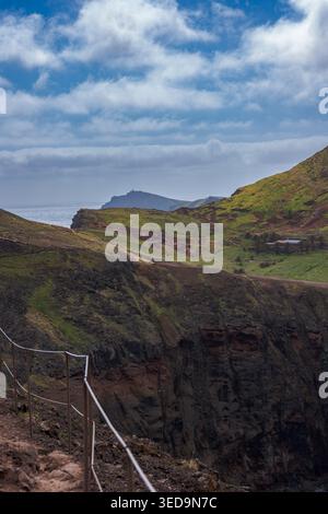 Dramatische Küstenlandschaft auf Madeira mit moosbedeckten vulkanischen Klippen, üppigen grünen Hügeln und Blick auf das ferne Meer unter einem hellen Stockfoto
