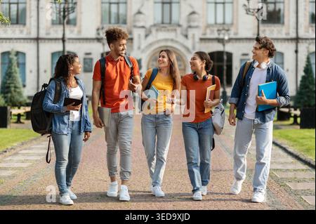 Glückliche Universitätsstudenten gehen zusammen auf dem Campus, plaudern und lachen Stockfoto