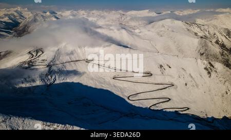 Aus der Vogelperspektive des Babusar Pass, der sich durch schneebedeckte Berggipfel unter einer Wolkenschicht schlängelt. Babusar, KPK, Pakistan. Stockfoto