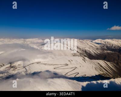 Aus der Vogelperspektive auf die gewundene Straße des Babusar Pass durch schneebedeckte Berggipfel unter einem klaren blauen Himmel in Babusar, KPK, Pakistan. Stockfoto